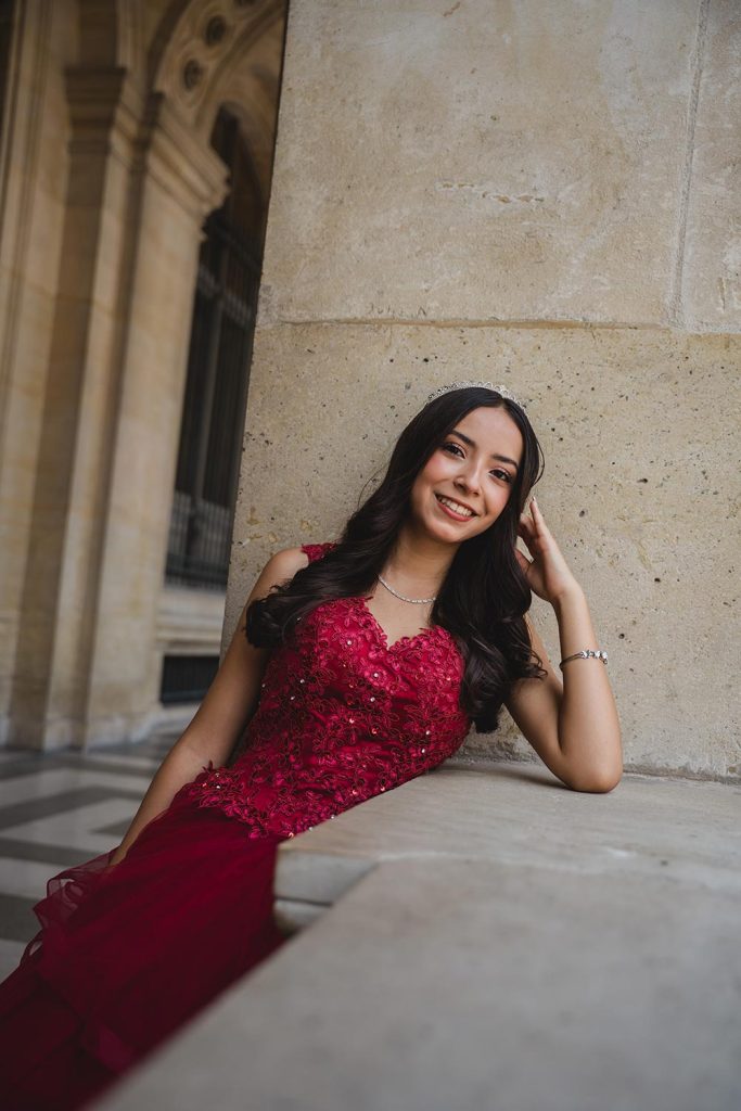 Retrato de quinceañera sonriendo con vestido rojo de encaje y corona en el Louvre, París / Portrait of a smiling quinceañera in a red lace dress and crown at the Louvre, Paris