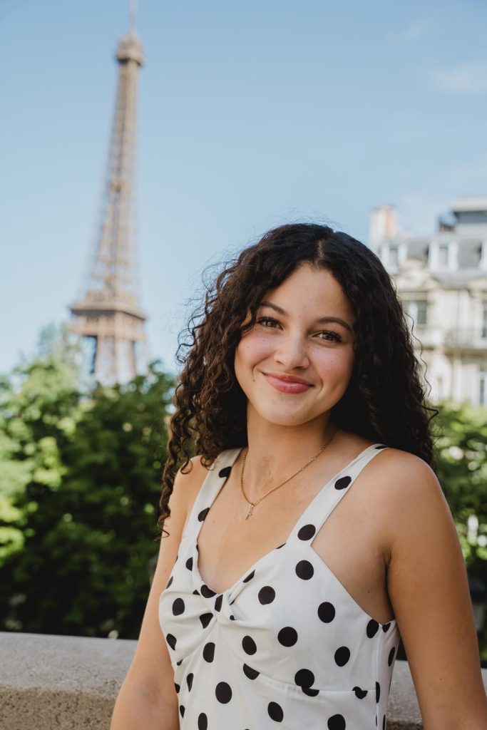 Retrato de quinceañera de cabello rizado sonriendo con vestido casual de lunares y la Torre Eiffel de fondo / Portrait of a curly-haired quinceañera smiling in a casual polka dot dress with the Eiffel Tower behind