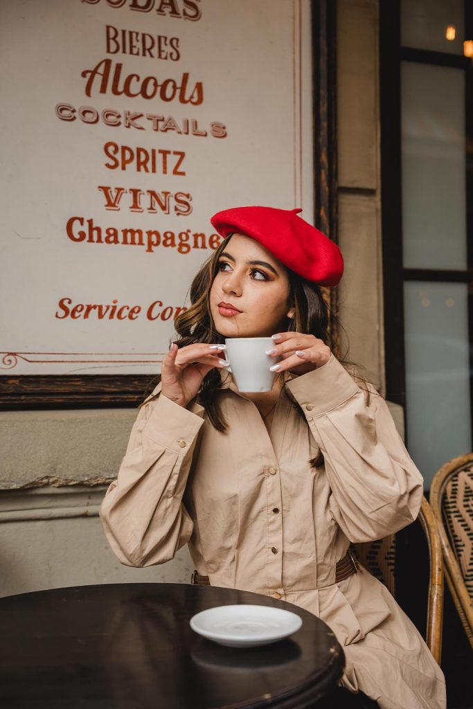 Quinceañera con boina roja y trench beige tomando café en una terraza parisina clásica / Quinceañera in a red beret and beige trench coat having coffee on a classic Parisian terrace