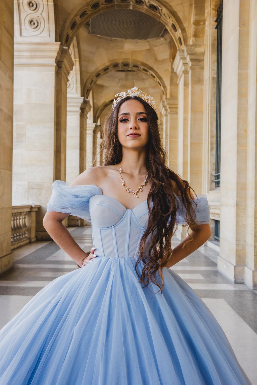 Quinceañera con vestido azul cielo estilo princesa y corona floral posando en las arcadas del Palais Royal en París / Quinceañera in a princess-style sky blue gown and floral crown posing in the Palais Royal arcades in Paris
